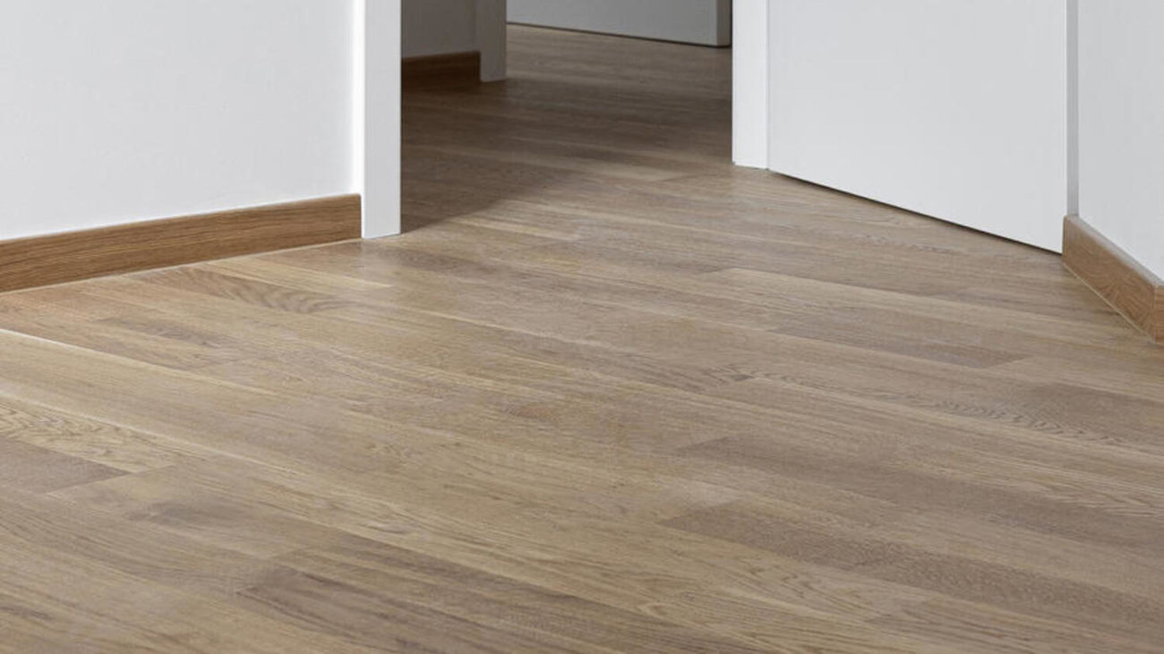 Паркетная доска Tarkett Oak Essence в интерьере коридора с деревянным плинтусом, белыми стенами и открытыми дверными проемами.