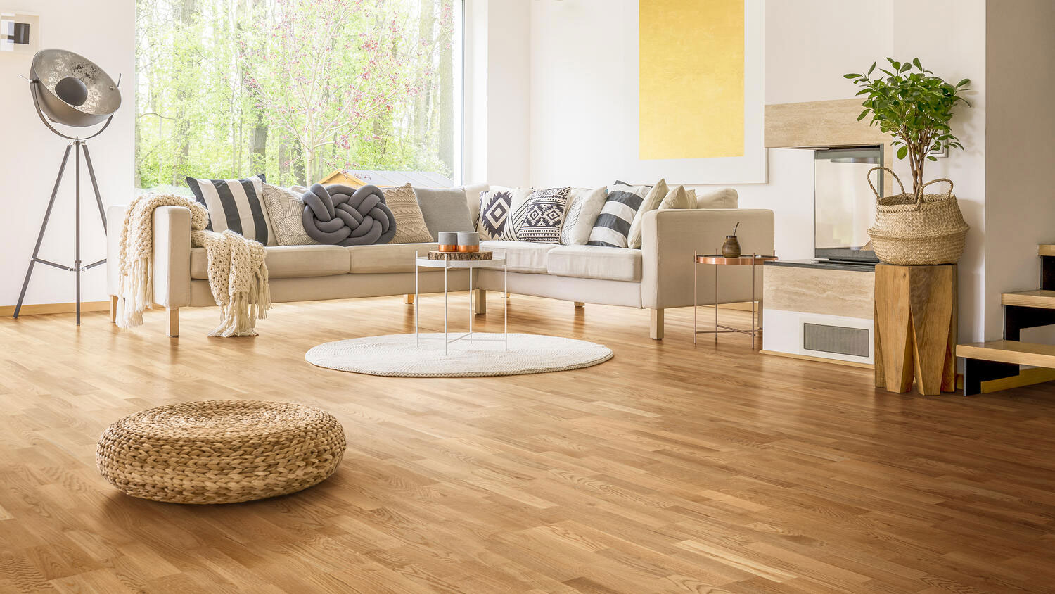 Паркетная доска Tarkett Classic Oak Baikal трехполосная в светлом сканди-интерьере гостиной с белым диваном, подушками и плетеным пуфом.