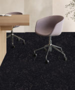 Ковровая плитка Desso Retrace черного цвета в офисном интерьере с деревянным рабочим столом и серыми эргономичными креслами на колесиках.