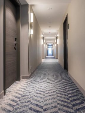 Ковровое покрытие в отеле Courtyard в интерьере длинного гостиничного коридора с сине-серым геометрическим узором шеврон и дверями номеров