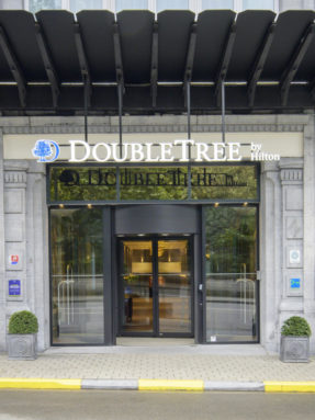 Напольное покрытие Tarkett в экстерьере у входа в отель DoubleTree by Hilton с панорамными стеклянными дверями и декоративными деревьями.