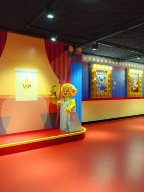Красный линолеум Tarkett в интерьере VIP-зоны LEGO с подиумом, ростовыми фигурами кинозвезд и светящимися афишами на стенах.