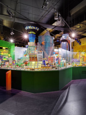 Темно-фиолетовый линолеум Tarkett в интерьере выставочного зала LEGO с огромным макетом города и небоскребов за стеклянным ограждением.