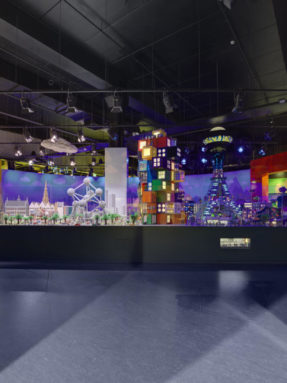 Темно-серый линолеум Tarkett в интерьере масштабной выставки LEGO с детализированным макетом города и футуристичных башен под стеклом.