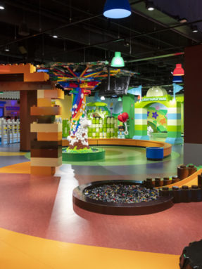 Разноцветный линолеум Tarkett в интерьере парка развлечений LEGO Duplo Park с декоративным деревом, арками и бассейнами из кубиков.