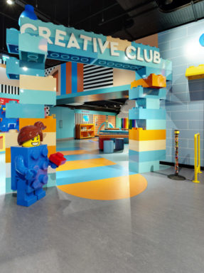 Серый и голубой линолеум Tarkett в интерьере игровой зоны LEGO Creative Club с большими кубиками конструктора и фигурой человечка.