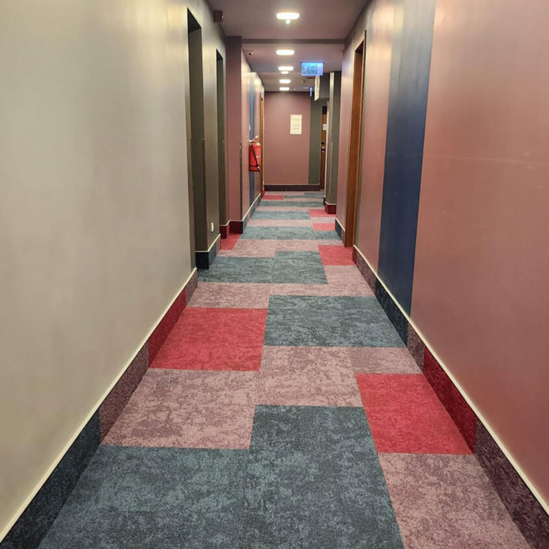 Ковровая плитка DESSO в интерьере коридора отеля Mercure Riga Centre Hotel с разноцветным геометрическим узором из серых, синих и красных квадратов