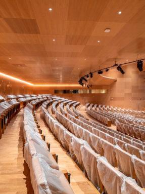 Деревянные стеновые и потолочные панели в интерьере зала Palais des congres 07 с рядами кресел в защитных чехлах и подсветкой стен