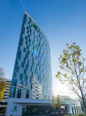 Напольные покрытия Tarkett на объекте Holiday Inn Hamburg - City Nord — вид на высотное застекленное здание отеля современной архитектуры.
