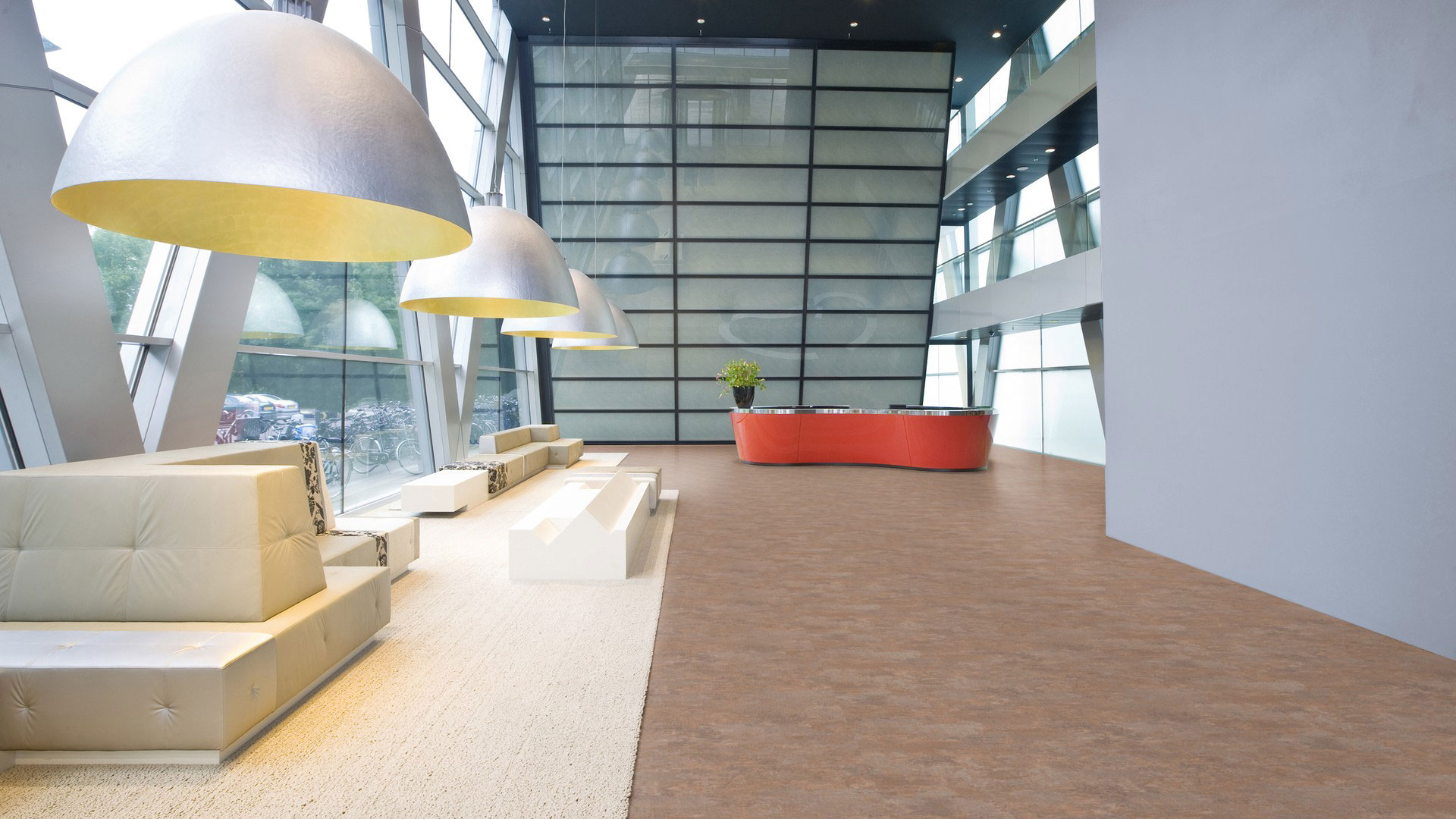 Линолеум Tarkett Excellence Carpet Brick коричневого цвета в интерьере просторного лобби с мягкими диванами, полусферическими светильниками и стойкой ресепшен