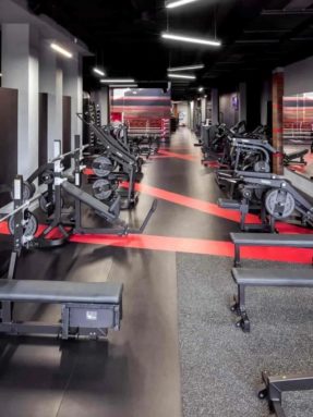 Черное спортивное покрытие Tarkett Omnisports в интерьере зоны свободных весов World Class со штангами, гантелями, скамьями и красной разметкой