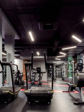 Черное спортивное покрытие Tarkett Omnisports в интерьере тренажерного зала World Class с механическими беговыми дорожками и гребными тренажерами