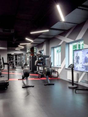 Черное спортивное покрытие Tarkett Omnisports в интерьере тренажерного зала World Class с беговыми дорожками, тренажерами и ТВ-экраном
