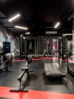 Черное спортивное покрытие Tarkett Omnisports в интерьере зала World Class с механическими беговыми дорожками, гребными тренажерами и красной разметкой