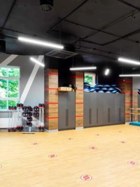 Спортивное покрытие Tarkett Omnisports под дерево в интерьере зала World Class для фитнеса со степ-платформами, гантелями и хореографическим станком