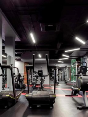 Черное спортивное покрытие Tarkett Omnisports в интерьере тренажерного зала World Class с механическими беговыми дорожками и гребными тренажерами
