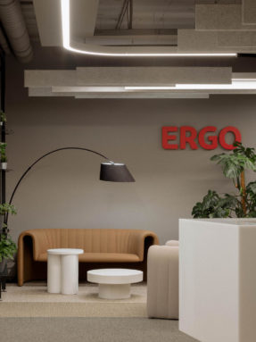 Ковровая плитка Desso в интерьере зоны ожидания офиса Ergo с кожаным диваном, журнальными столиками, торшером и красным логотипом.