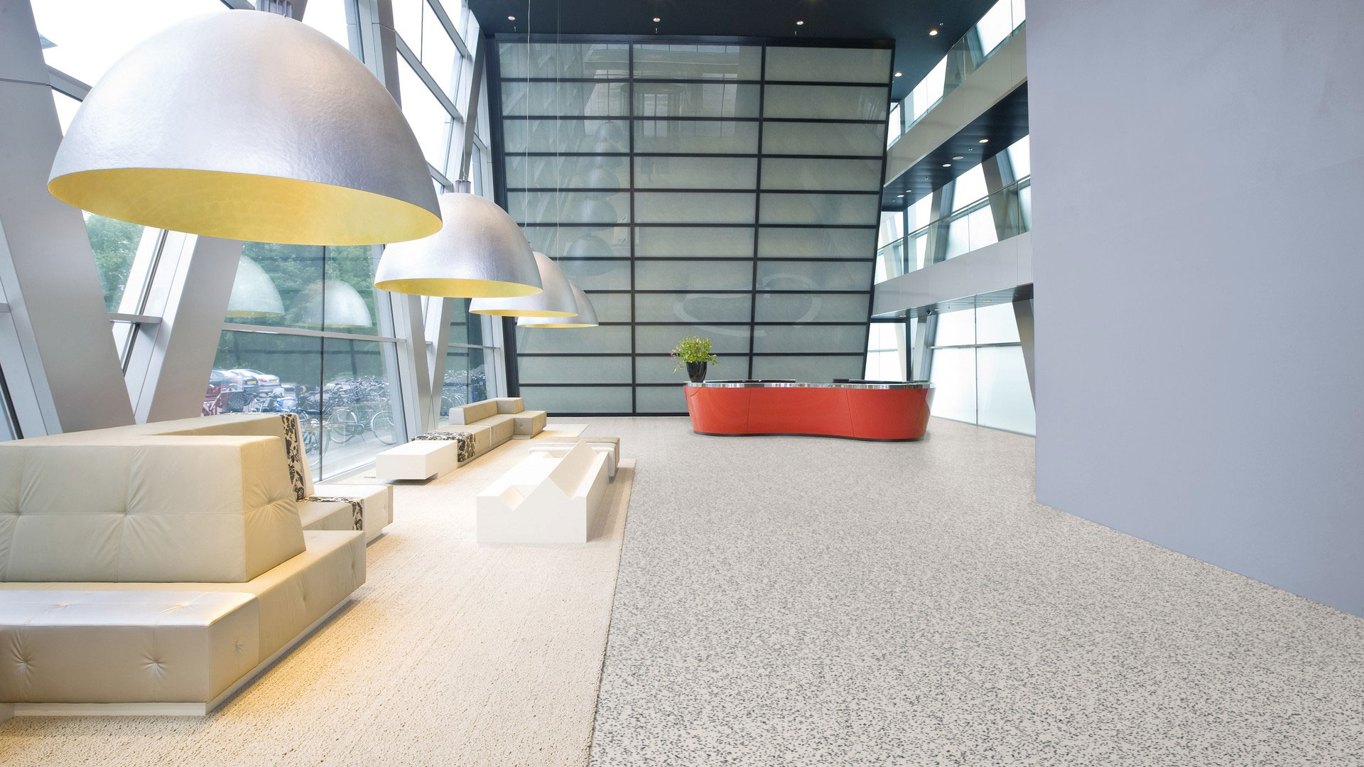 Гомогенный линолеум Tarkett iQ Surface 083 Contrast Airy в просторном интерьере офисного холла со светлыми диванами, большими полусферическими лампами и стойкой ресепшн.