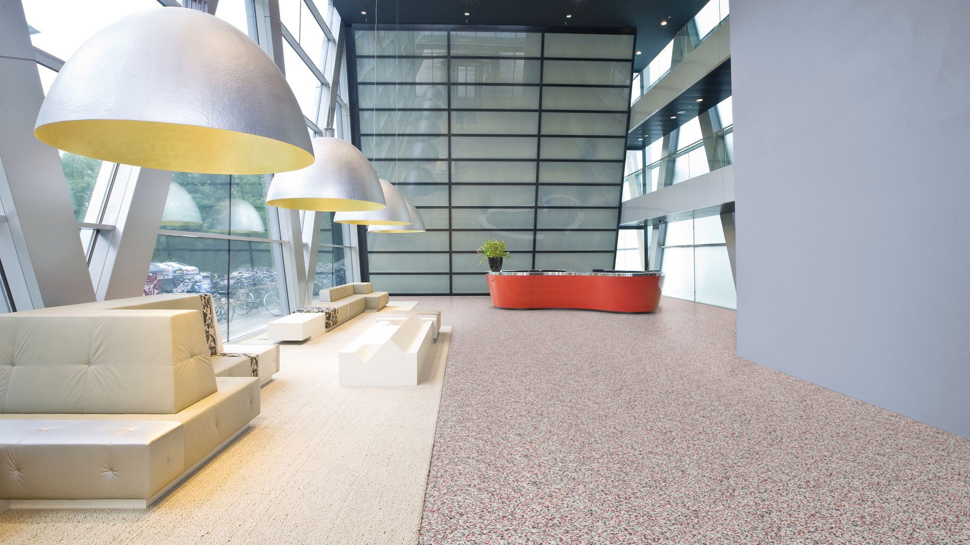 Гомогенный линолеум Tarkett iQ Surface 089 Vivid Airy в просторном интерьере офисного холла с большими полусферическими лампами и стойкой ресепшн.